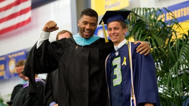 Seattle Seahawks quarterback Russell Wilson (left) poses enthusiastically after The Pine School graduating senior A.J. Lettengarver reveals Wilson's jersey under his gown during the graduation commencement Saturday at the Hobe Sound campus. Katie Rodgers, whose father Mark Rodgers represents Wilson, invited the Super Bowl winner to speak during the ceremonies. Go to TCPalm.com to see more photos. (XAVIER MASCARE-AS/TREASURE COAST NEWSPAPERS) CQ:A.J. Lettengarver, Russell Wilson, Mark Rodgers, Katie Rodgers DATE TAKEN:053015